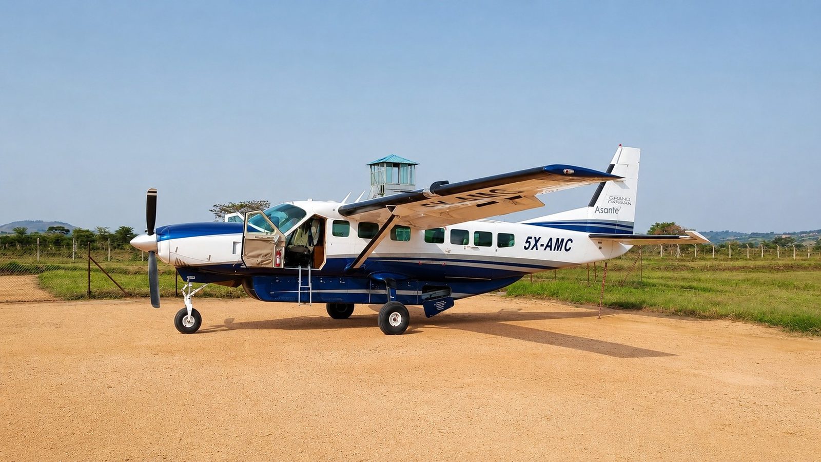 Asante Aviation Cessna Grand Caravan 5X-AMC parked on a dirt strip, control tower behind